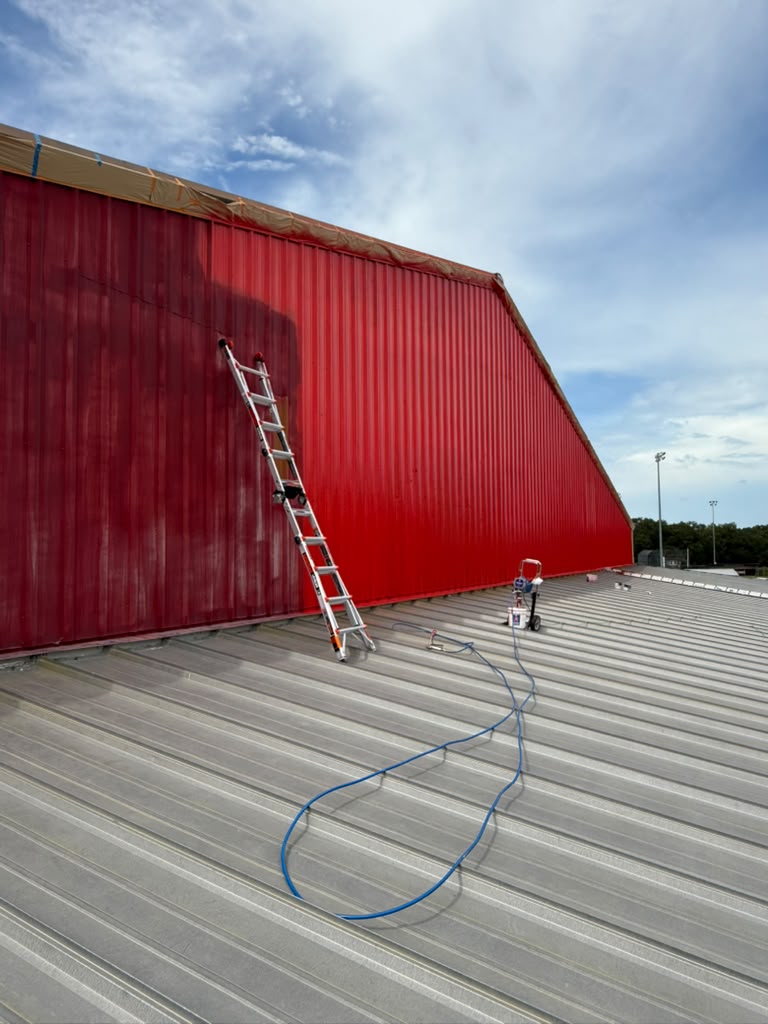 Crew painting a metal building exterior from a ladder
